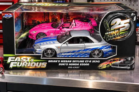 Fast and Furious 25th anniversary Jada Toys die-cast set in its display box on a workshop bench, a silver and blue Nissan Skyline GT-R R34 and a pink Honda S2000